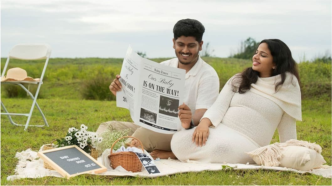 Couple reading a mock newspaper announcing their pregnancy in a meadow