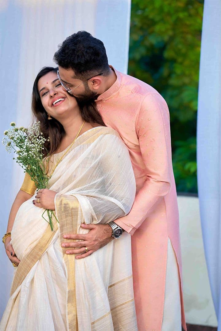 Traditional maternity portrait of a couple, pink silk saree, soft curtains