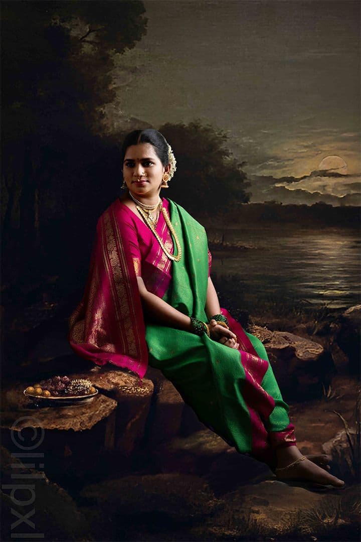 Traditional maternity portrait in a green and pink silk saree, painterly backdrop