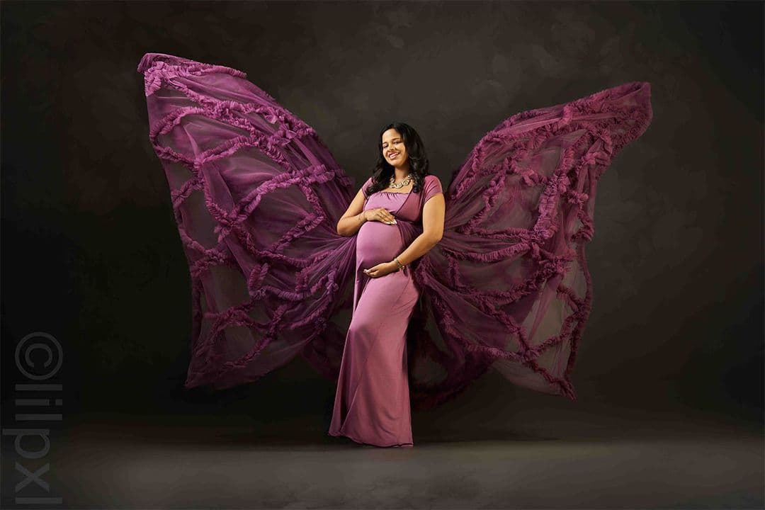 Maternity portrait with dramatic flowing purple tulle wings, fine-art studio lighting