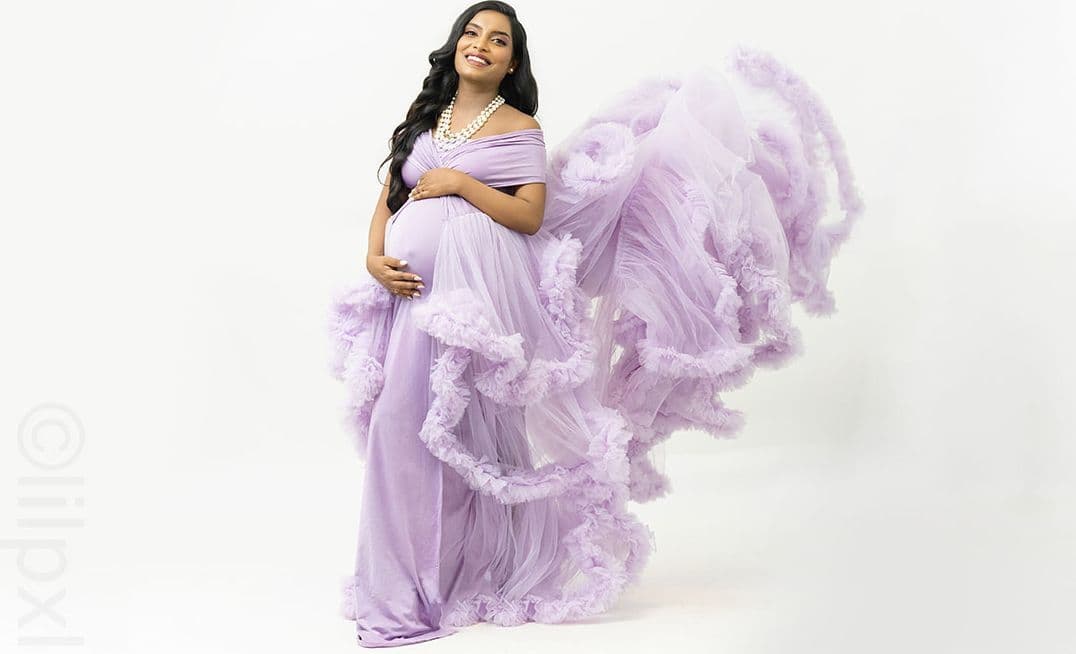 Maternity portrait in a lavender gown with tulle swept mid-air, studio