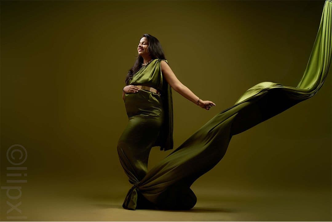Maternity portrait in flowing emerald satin, moody studio light