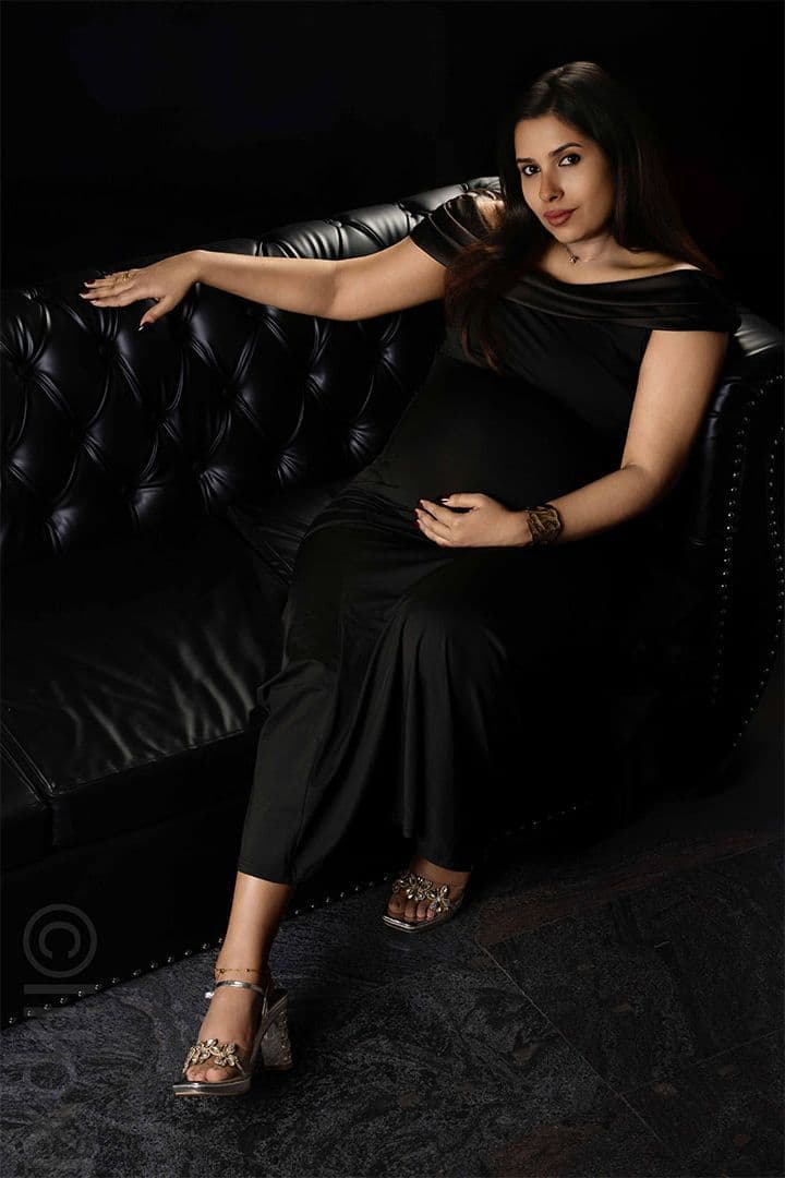 Maternity portrait in a black gown on a tufted leather sofa